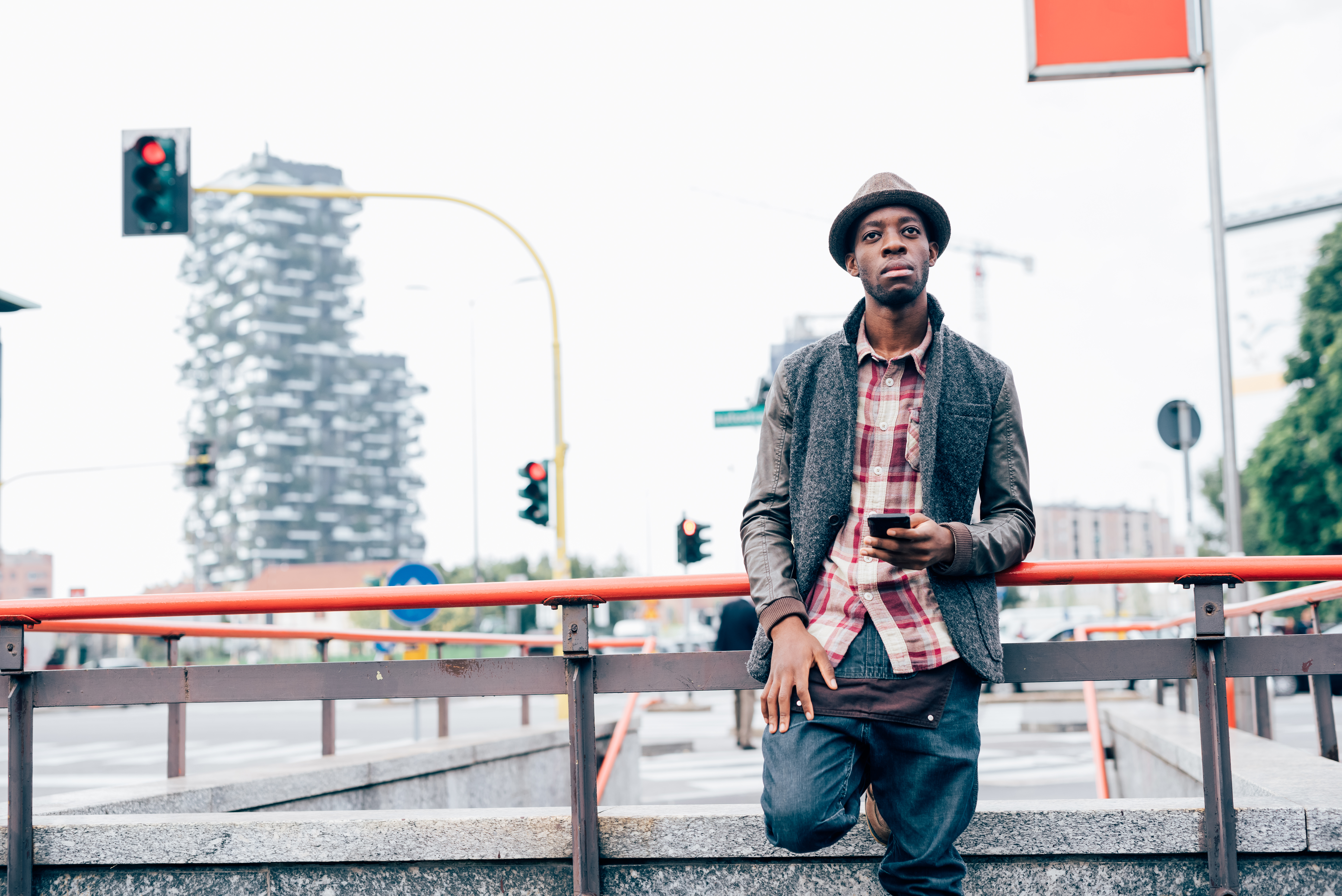 knee-figure-of-young-handsome-afro-black-man-PK3PDEA Knee figure of young handsome afro black man leaning on a handrail, holding a smart phone, looking over pensive- technology, social network, communication concept